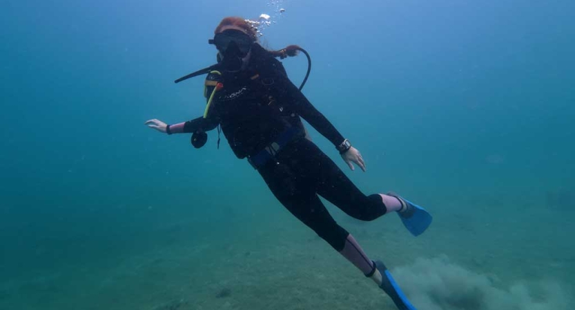 A person in a wet suit scuba dives in rich blue water